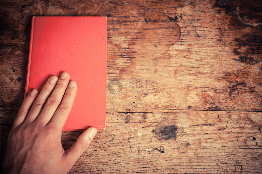 个人把左手放桌子旁的本红色的书上图片