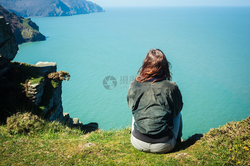 轻的女人坐海边的悬崖边上图片