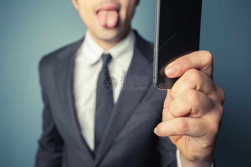 轻的商人正用他的智能手机自拍,伸出舌头图片