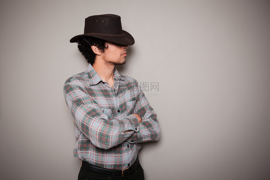 个戴着牛仔帽格子衬衫的轻人正着绿色的墙壁摆姿势图片