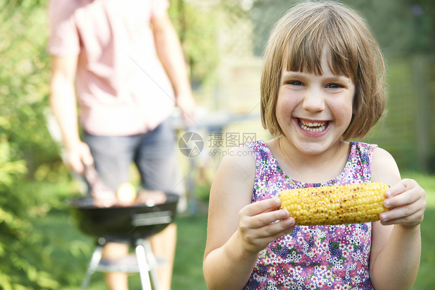 轻女孩家庭烧烤时吃甜玉米图片
