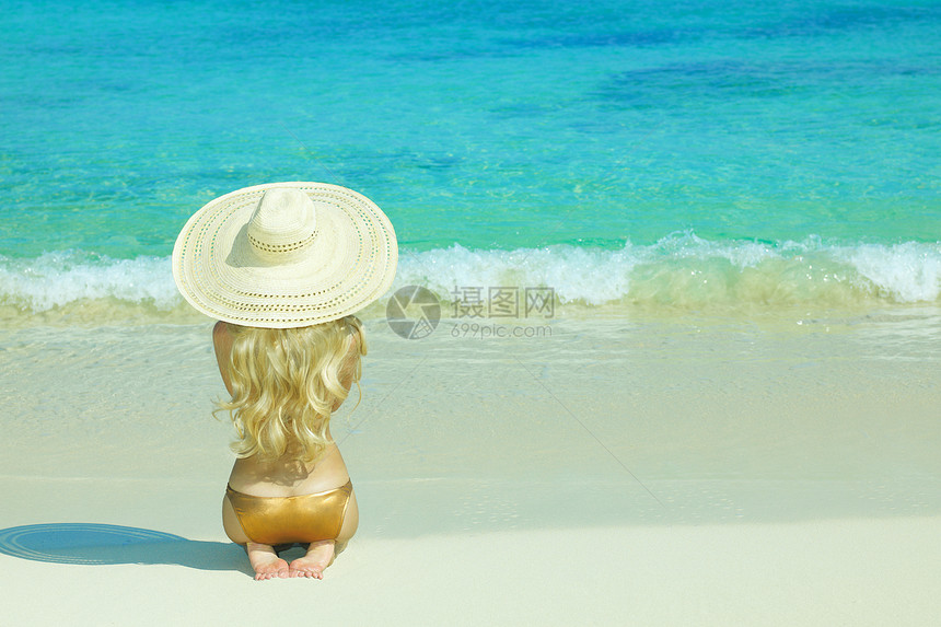 优雅的轻女人戴着帽子坐海滩上图片