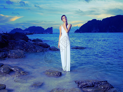 美丽的女士穿着白色的连衣裙岩石海岸上图片