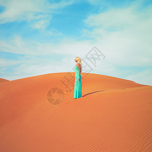 美丽的金发女郎穿着蓝色的连衣裙,穿着橙色的沙漠阿联酋图片