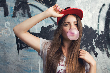泡泡糖女孩时尚美丽的长发模特涂鸦背景上摆姿势泡泡,竖大拇指红色帽子灰色T恤背景