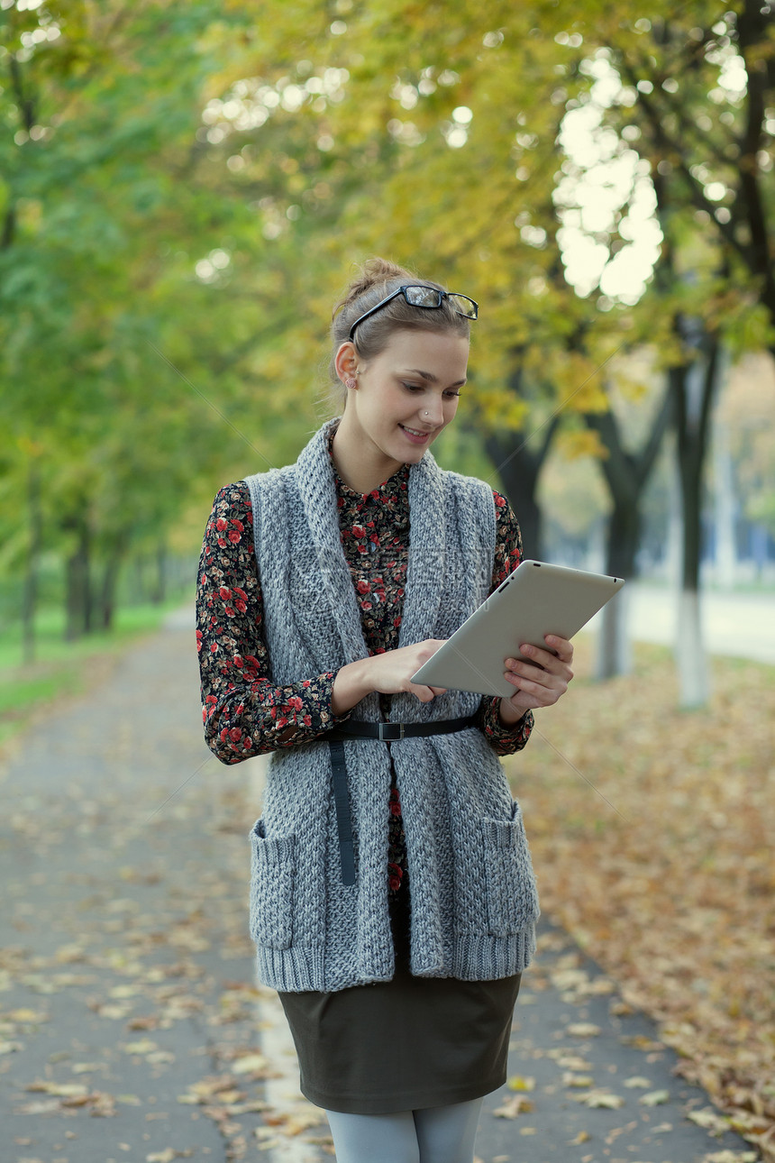 时尚风格的轻女秋天的街道上用平板电脑图片