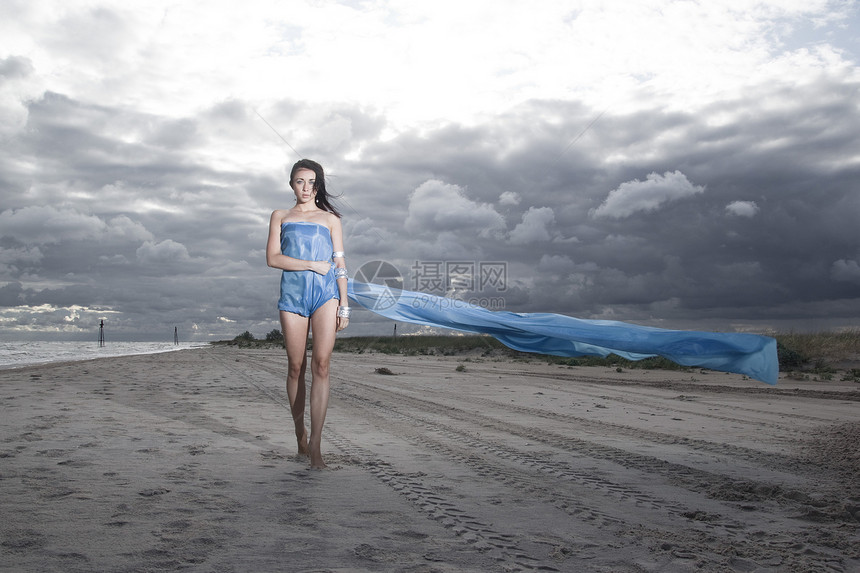 海滩上穿着蓝色长裙的漂亮模特多风多云的夏季天气图片