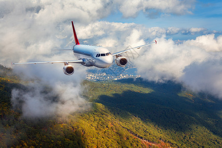 日落时,飞机云层中飞过森林风景与白色客机,多云的天空绿树客机正降落商务旅行商业飞机背景图片