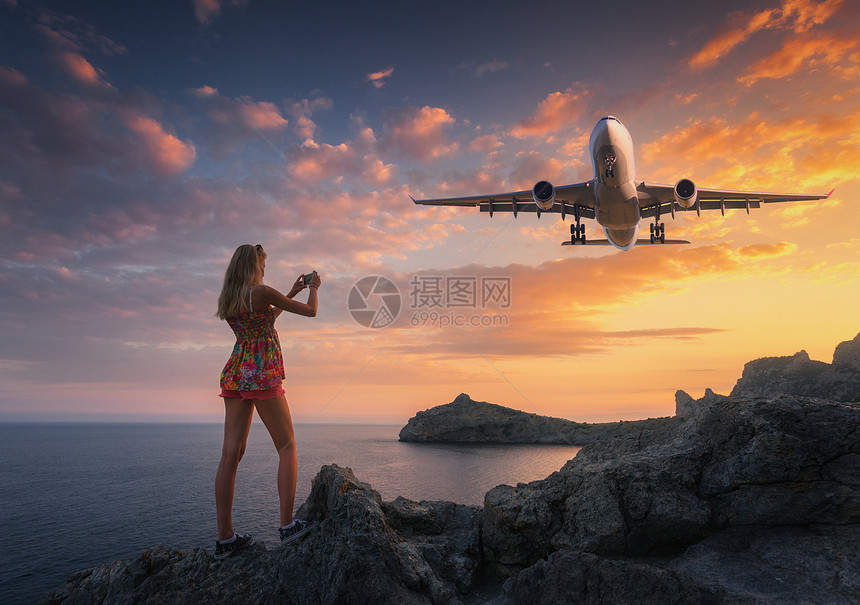 美丽的女人日落时拍摄着陆飞机的照片夏天的风景,女孩站岩石上,乘客机五彩缤纷的天空下飞行女人降落的商业飞机图片