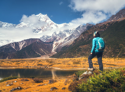 站着的轻女人,背着背包石头上,看着夕阳下的群山风景与女孩,高岩石与雪峰,黄草,蓝天尼泊尔旅行徒步旅行背景图片