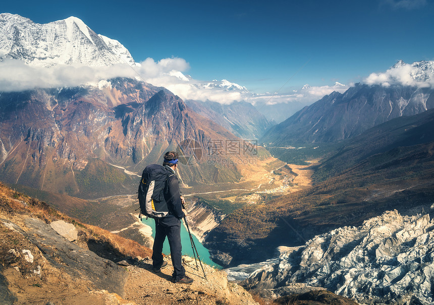 站着运动的人,背包山峰上,日落时看着美丽的山谷风景与人,岩石与雪峰,冰川,云尼泊尔徒步旅行徒步旅行站山顶上图片