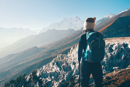 比利茨基高峰站山顶上背着背包的轻女人,日落时看着美丽的山谷风景与女孩,岩石与雪峰,山丘,蓝天尼泊尔徒步旅行,旅行老式背景