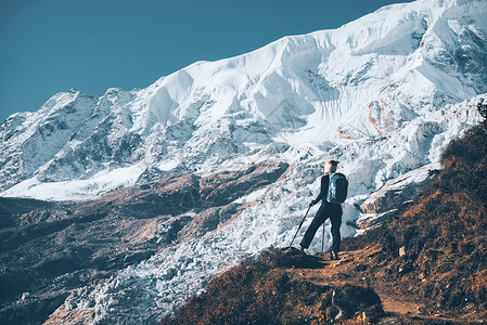 比利茨基高峰站山顶上背着背包的轻女人,日落时看着美丽的山脉冰川风景与女孩,岩石与雪峰,蓝天尼泊尔徒步旅行,旅行古董背景