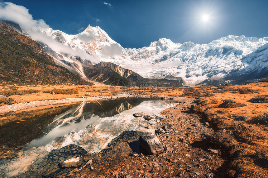 美丽的景色高高的岩石,雪覆盖着山峰,山湖里的石头,水中的倒影,日落时的蓝天尼泊尔美丽的风景与喜马拉雅山脉明亮的晴天图片