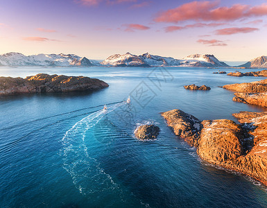 海 货船鸟瞰渔船,蓝色海洋中的岩石,雪山五颜六色的紫色天空,冬季的黄昏,挪威洛弗滕岛,两艘船的景观的风景旅行背景