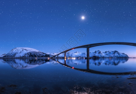 比利茨基星星神奇的桥星空,美丽的倒影水中夜风景与桥,雪山,蓝天与月亮明亮的星星反射海上挪威洛福滕岛的冬天背景