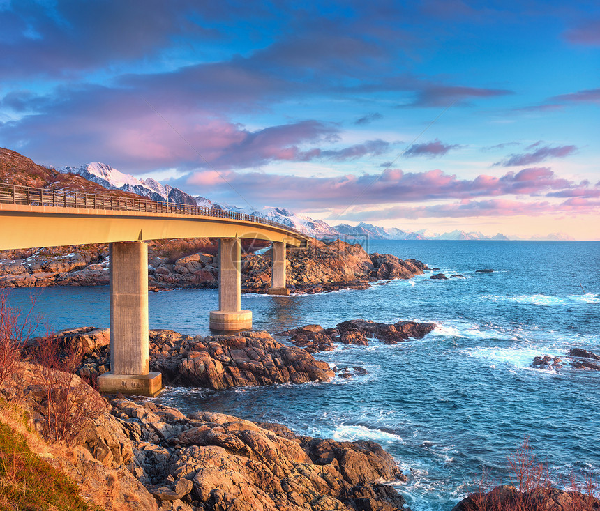 挪威洛福腾群岛日出时美丽的桥神奇的景观与桥梁,五彩缤纷的天空与紫色的云,雪山,岩石,蓝色的海洋与波浪春天欧洲旅行图片