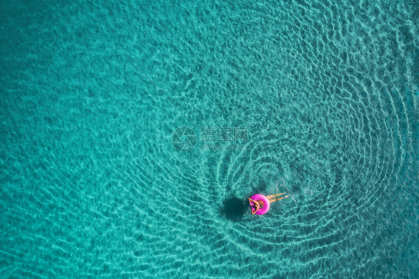 轻女子粉红色游泳圈上游泳的鸟瞰图泰国日出时,轻女子透明的绿松石海中游泳的粉红色游泳圈上的鸟瞰夏天的海景与女孩,图片