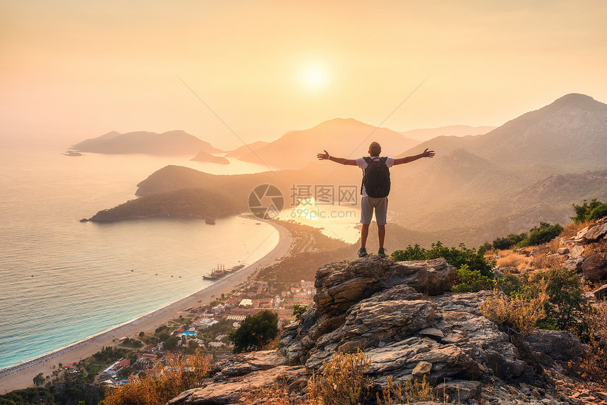 快乐的运动男人,带着背包,举手臂,站岩石上,夏天的日落时看着海岸山脉人,海,山脊橙色的天空奥卢德尼斯,火鸡图片