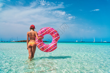 美丽的轻女子穿着橙色比基尼,粉红色甜甜圈游泳环透明的海洋阳光明媚的夏天热带景观感的苗条女孩的背部,清澈的水,蓝天背景图片