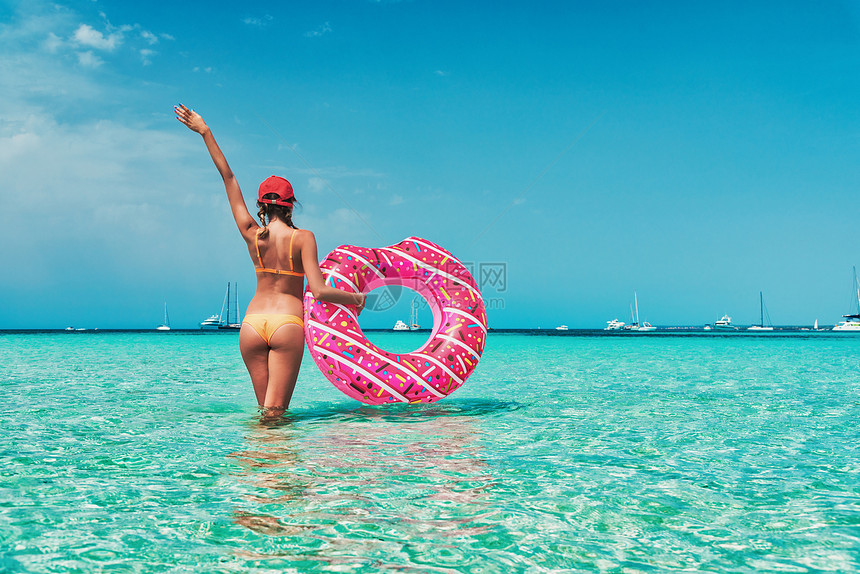 美丽的轻女子穿着橙色比基尼,粉红色甜甜圈游泳环透明的海洋阳光明媚的夏天热带景观感的苗条女孩的背部,清澈的水,蓝天图片