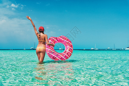 美丽的轻女子穿着橙色比基尼,粉红色甜甜圈游泳环透明的海洋阳光明媚的夏天热带景观感的苗条女孩的背部,清澈的水,蓝天背景图片