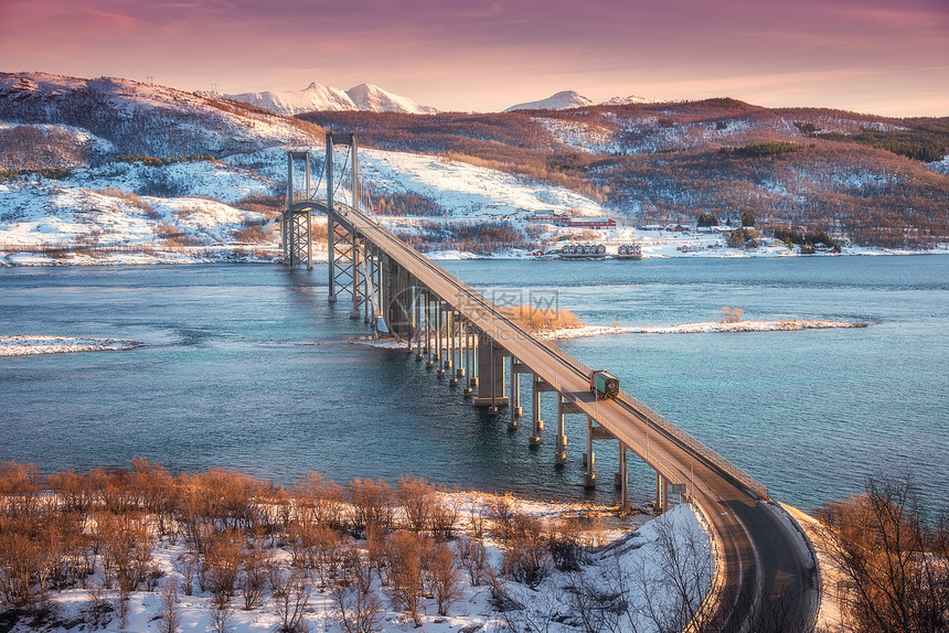 挪威洛福滕群岛日落时的美丽桥梁空中冬季景观与汽车路上,蓝色的大海,树木,雪山,五颜六色的红色天空与云彩,建筑物北欧的风图片