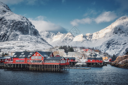 挪威洛福腾群岛的小村庄里,红色的传统RorBuer冬天的日落时风景蓝海,雪山,建筑,多云的天空美丽的罗布高高的岩图片