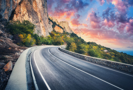 日落时的山路美丽的天空五颜六色的景观,高岩石,蜿蜒的沥青路,树木蓝天与红色橙色的云秋天旅行山中高速公路的风背景图片
