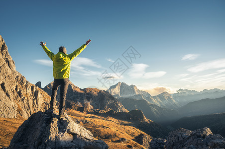 比利茨基幸福的运动的人站石头上,举手臂日落时抗山谷快乐的轻人,岩石,秋天的森林蓝天白云石,意大利旅行者高山上徒步旅行背景