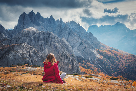 轻的女人正坐山上,秋天的白云石,意大利的壮丽的山风景与女孩,多云的天空,橙色的草,高岩石与森林秋天意大利阿尔卑斯背景图片