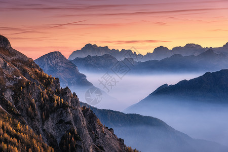 意大利白云石秋天美丽的日落时,雾中的山脉景观与高山山谷,低云,山上的树木,橙色的天空与云黄昏空中视野帕索贾乌背景图片