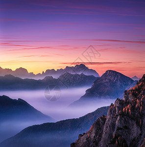 意大利白云石秋天美丽的日落时,雾中的山脉景观与高山山谷,低云,树木山上,紫色的天空与云黄昏空中视野帕索贾乌背景图片