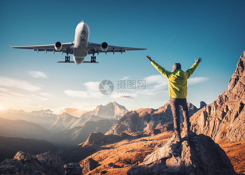 飞机人石头上举手臂,日落时抗山谷快乐的轻人,飞行的客机,岩石蓝天白云石,意大利旅行者着陆飞机图片
