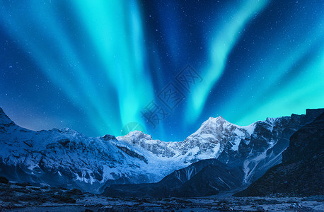 比利茨基盖满欧洲雪覆盖山脉上方的北极光冬天的北极光夜间景观与绿色极地灯雪山星空,岩石上极光背景
