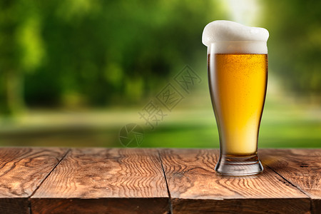 啤酒木制桌子上的璃与模糊的城市公园的背景,自然背景与Bokeh图片