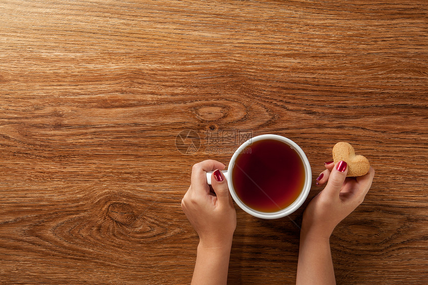女人着杯热茶,木桌上放着饼干图片