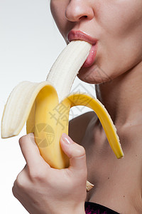 轻的女人咬香蕉隔离白色图片