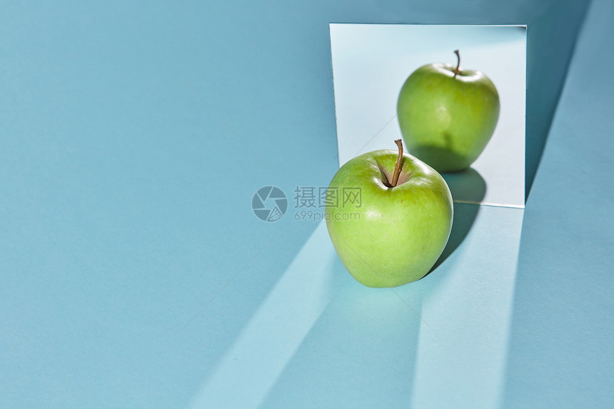 镜子里整个绿色苹果的倒影镜子里苹果的影子蓝色桌子表的镜子苹果的长影苹果绿色的,蓝色背景上的方形镜子,苹果的反射镜图片
