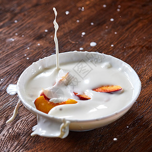 桃子酸奶牛奶酸奶溅同的方向,成熟的桃子水果掉进陶瓷碗里准备顿美味健康的早餐片成熟的新鲜桃子落陶瓷碗里,张木桌上放了背景