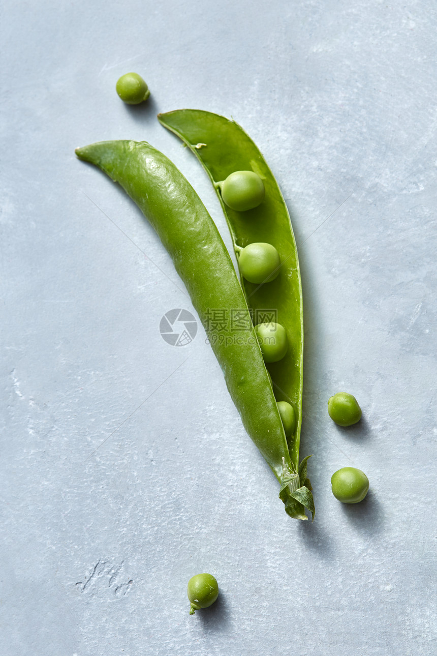 天然素食清洁生食绿色豌豆的棍子灰色的桌子上,顶部的景色天然机豌豆的荚开放的,灰色的背景上小的球形颗粒图片