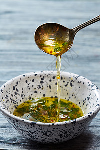 刚准备好的沙拉酱勺子里掉进陶瓷碗里,灰色的木制背景上放着橄榄油切碎的草药盐胡椒醋用橄榄油醋蔬菜香料自制的沙拉图片