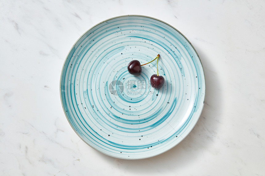 美味的夏季天然新鲜水果樱桃蓝色盘子上清洁机饮食的平躺两个成熟的甜暗红色樱桃个蓝色陶瓷盘子灰色的石头背景图片