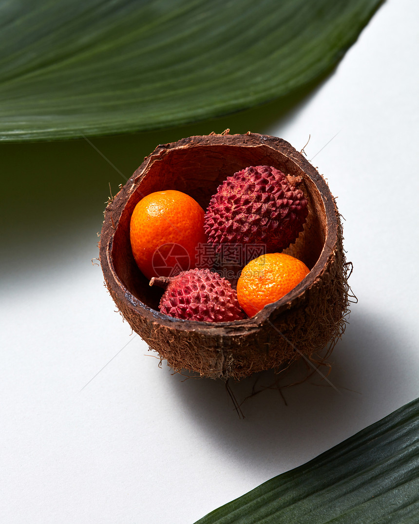 热带异国水果莱奇金橘椰子壳与常青叶分离白色背景特写照片椰壳中Lytchi金橘果实的特写,白色背景上分离出热带绿叶图片