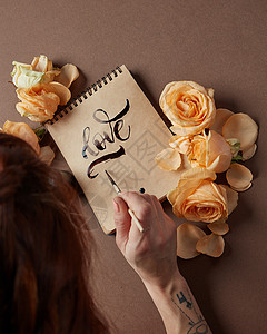轻女人用刷子写爱字的背景装饰着鲜花用画笔写情书图片