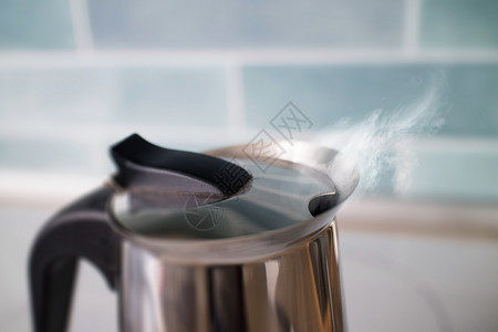 圣洁水锅炉茶壶与沸腾的热气腾腾的饮用水蒸汽它的蓝色瓷砖厨房水壶用沸腾的热气腾腾的饮用水蒸汽背景
