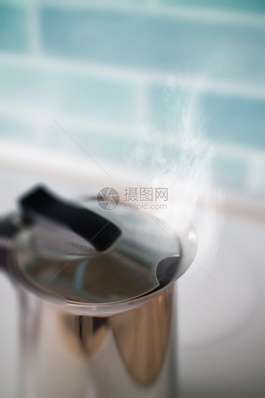 蒸汽厨房蓝色瓷砖的背景上的铁水壶里冒出来茶壶用开水抵厨房的蓝色瓷砖上图片