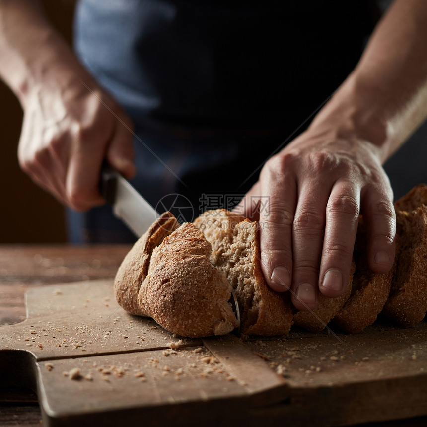 雄的手木板上切小麦包关门健康的饮食传统的烘焙理念男手切小麦包,特写图片