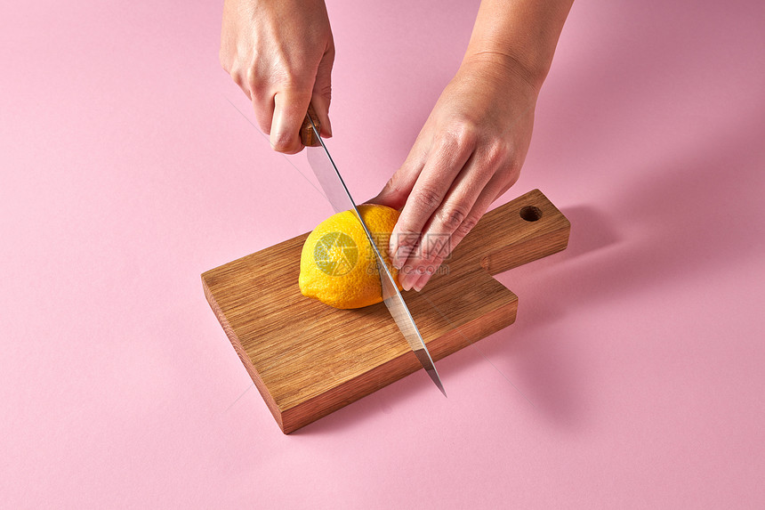 砧板上的柑橘类水果女的手粉红色背景的木板上把黄色成熟的柠檬切成两半素食女孩的手粉红色背景的木板上把黄色成熟的图片
