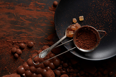 黑色碎片勺子与糖果可可粉个筛子上的黑色盘子,黑色背景与巧克力糖果可可粉背景